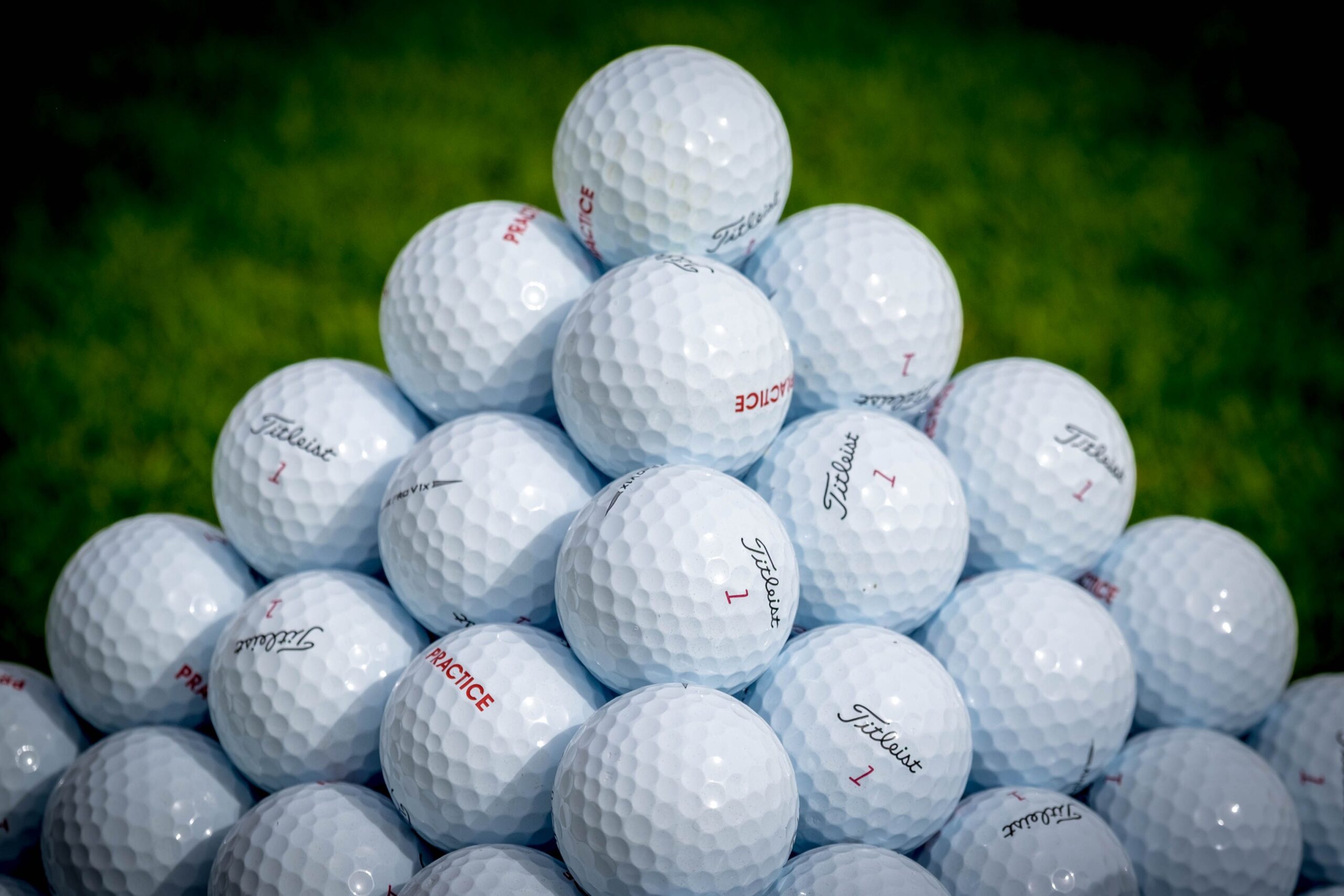 Close-up of stacked white golf balls forming a pyramid on green grass.